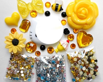 May include: A set of yellow and white embellishments for crafting, including a sunflower, a rose, a bow, a bee, a Hello Kitty face, and various rhinestones and beads.