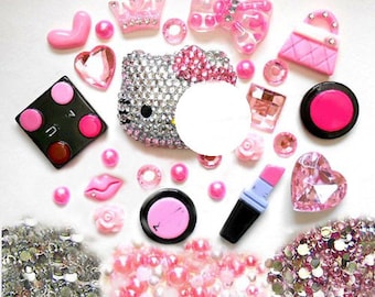 May include: A collection of pink and white rhinestones, glitter, and other decorative embellishments, including a Hello Kitty-inspired character, a small purse, and a lipstick tube.