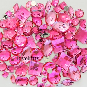 May include: A large assortment of pink rhinestone embellishments in various shapes and sizes. The rhinestones are perfect for adding sparkle to crafts, clothing, and home decor.