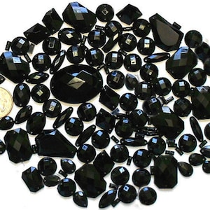 May include: A large assortment of black glass rhinestones in various shapes and sizes. The rhinestones are scattered on a white background.