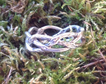 Könnte beinhalten: Ein silberner Ring mit einem gedrehten, astähnlichen Design. Der Ring liegt auf einem Hintergrund aus grünem Moos.