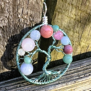 May include: A handcrafted pendant featuring a wire tree design with colorful gemstone beads. The pendant has a silver-colored bail and is made with green wire. The beads are various colors, including pink, blue, and green.