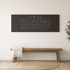 May include: A black rectangular wall art piece with white script that reads "love the Lord" and a Bible verse. Below, a wooden bench with a cream-colored throw and a round jute rug.