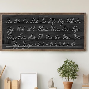 May include: A framed chalkboard with cursive handwriting of the alphabet and numbers 1-10. The word "PERMANSHIP" is at the top. The chalkboard has a dark gray background and a brown wooden frame.