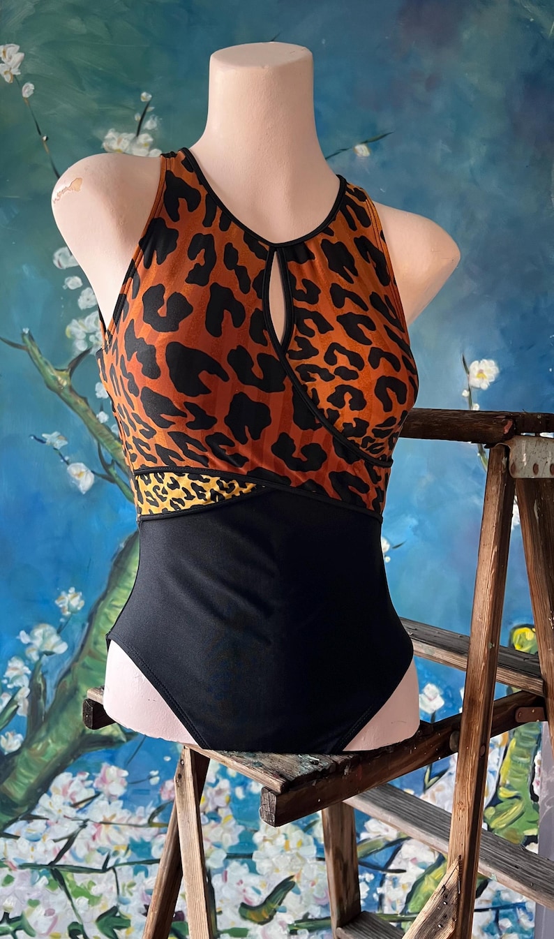 May include: A black and orange leopard print swimsuit with a keyhole cutout in the front. The swimsuit has a black bottom and a leopard print top with a black band.