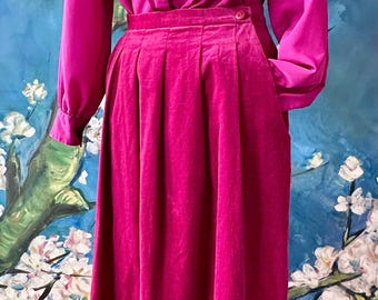 May include: A vibrant fuchsia velvet skirt and blouse set. The long-sleeved blouse has a button-down collar and the skirt is pleated with pockets. The set is a solid color and has a vintage aesthetic.