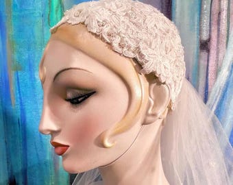 May include: A white lace cap headpiece featuring intricate floral embroidery and small pearl accents, paired with a sheer tulle veil. The headpiece is displayed on a mannequin head, showcasing the detailed lace texture and the delicate veil fabric.