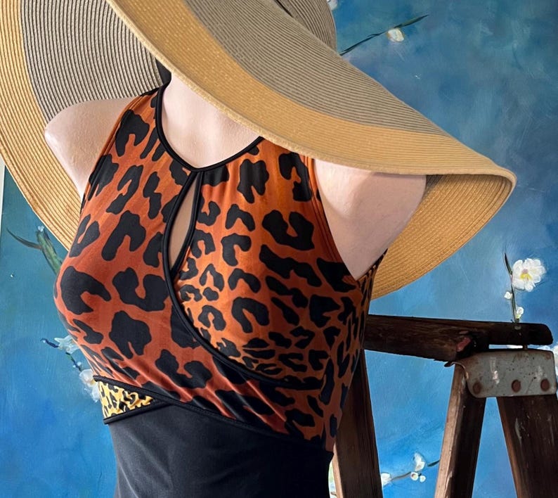May include: A brown and black leopard print halter top with a keyhole cutout in the front. The top is paired with a black skirt and a wide-brimmed straw hat.