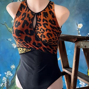 May include: A black and orange leopard print swimsuit with a keyhole cutout at the neckline. The swimsuit has a black bottom and a thin orange band at the waist.