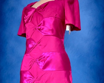 May include: A vibrant fuchsia dress featuring short sleeves, a square neckline, and a series of horizontal satin panels down the front. Each panel is gathered in the center to create a knotted effect. A white tag is attached to the sleeve.