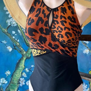 May include: A black and orange leopard print swimsuit with a keyhole cutout at the neckline. The swimsuit has a black bottom and a black band across the bust.