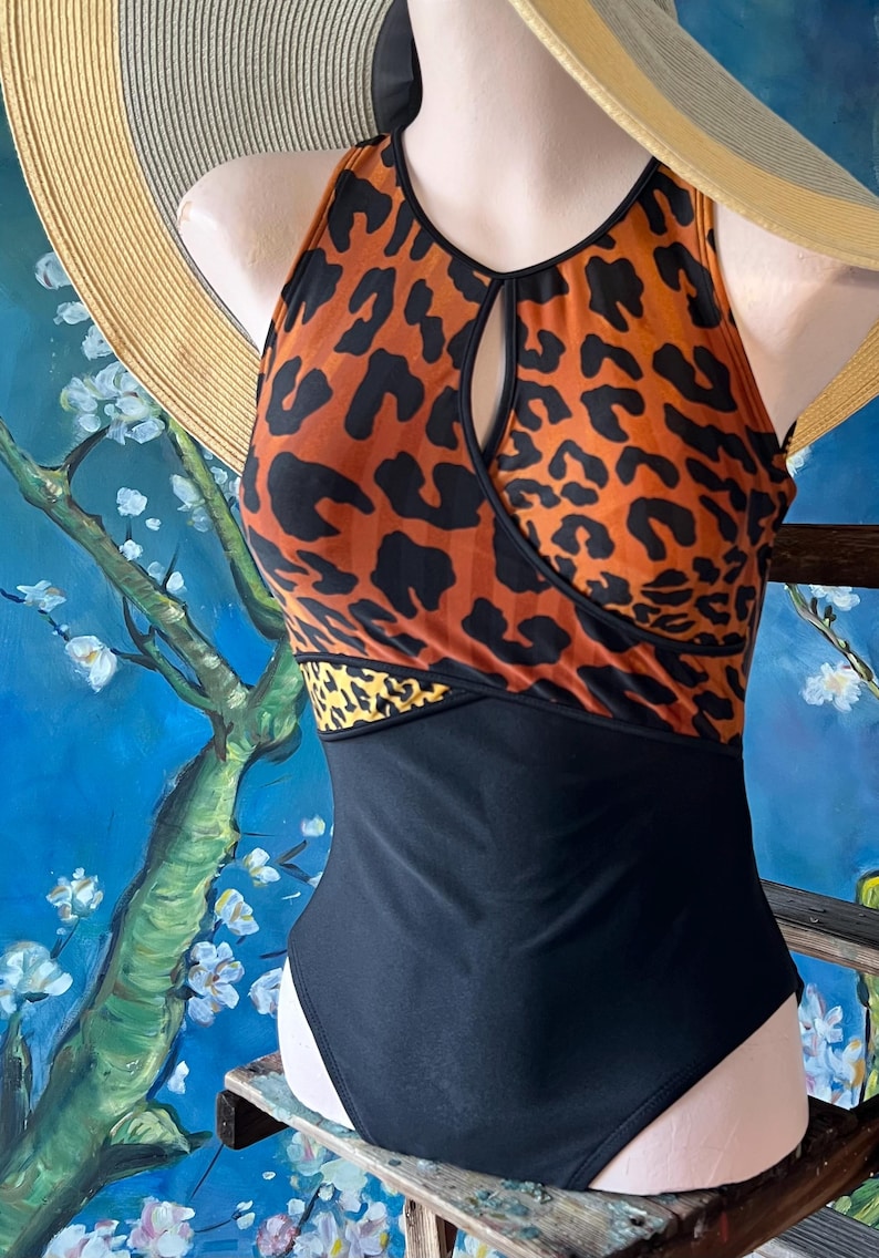 May include: A black and orange leopard print swimsuit with a keyhole cutout at the neckline. The swimsuit has a black bottom and a black band across the bust.