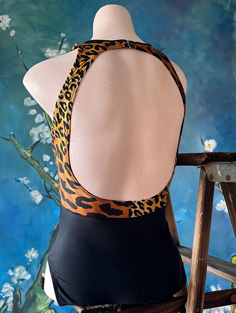 May include: Black swimsuit with a leopard print top and a black bottom. The swimsuit has a halter neck and a low back.
