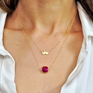 May include: A gold necklace with a small double heart charm and a larger, square-shaped, dark pink gemstone pendant.