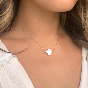 May include: A delicate gold chain necklace with a white, four-leaf clover pendant.