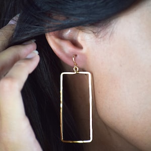 May include: Gold rectangle shaped dangle earrings. The earrings are hollow and have a hammered texture.
