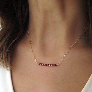 May include: A delicate gold chain necklace with a row of small, deep red gemstone beads.