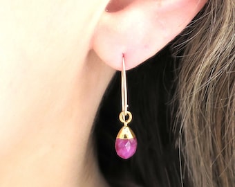 Pode incluir: Brincos de argola de ouro com uma gema rosa pendurada. Os brincos são usados na orelha de uma pessoa.