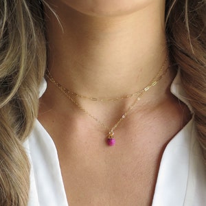 May include: A delicate gold chain necklace with a small, round, pink gemstone pendant.