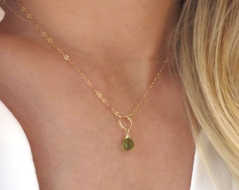 May include: A delicate gold chain necklace with a small, round, green gemstone pendant.