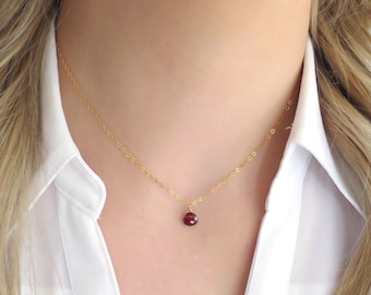 May include: A delicate gold chain necklace with a small, round, red gemstone pendant.