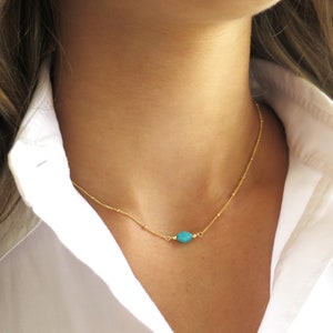 May include: A delicate gold chain necklace with a single turquoise gemstone pendant.