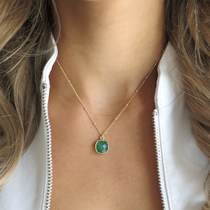 Puede incluir: Un collar de cadena dorada con un colgante de piedra preciosa verde. El colgante tiene forma cuadrada con bordes redondeados.