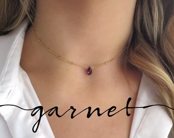 May include: A delicate gold chain choker necklace with a small teardrop-shaped garnet pendant.