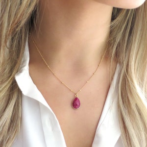 Può includere: Una collana con catena dorata e un ciondolo a forma di lacrima con una pietra rossa.