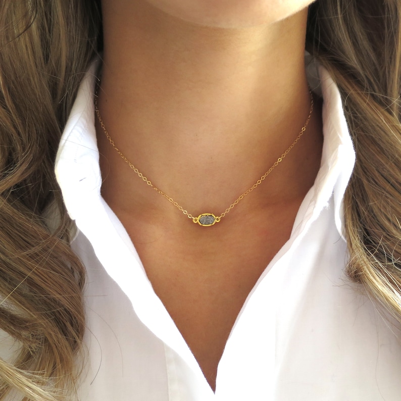 May include: A delicate gold chain necklace with a small, oval-shaped, grey gemstone pendant.