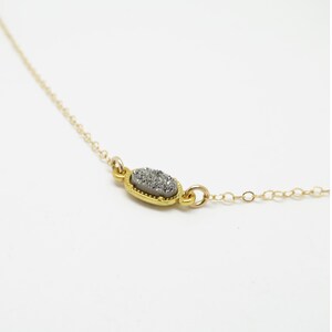 May include: A delicate gold chain necklace with a small oval pendant featuring a silver-grey druzy stone.