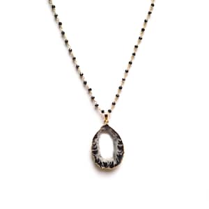 May include: A gold chain necklace with black beads and a large, oval-shaped pendant made of agate. The agate is a natural stone with a white center and a black outer edge.