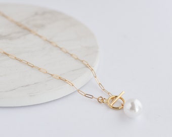 May include: A gold chain necklace with a toggle clasp and a single white pearl pendant.