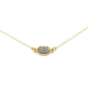 May include: A delicate gold chain necklace with a small oval pendant featuring a grey and white agate stone.