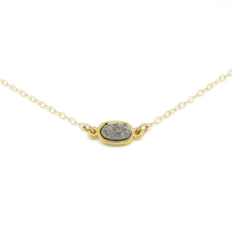 May include: A delicate gold chain necklace with a small oval pendant featuring a grey and white agate stone.