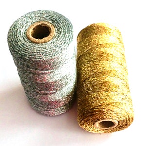 May include: Two spools of metallic thread, one silver and one gold. The spools are wound with thread and have a cardboard centre.