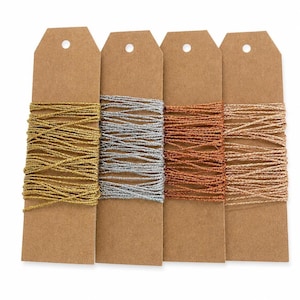 May include: Four rectangular brown cardboard tags, each featuring a circular hole at the top. Each tag is wrapped with a different metallic thread: one gold, one silver, one copper, and one rose gold, all wound horizontally around the card.