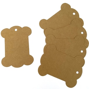 May include: A set of six brown paper spool-shaped gift tags with a hole punched in the top. The tags are ideal for adding a rustic touch to gifts.