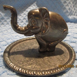 May include: Silver elephant ring holder with an ornate, engraved base. The elephant is standing on its hind legs with its trunk raised.