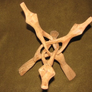 May include: A wooden stand with three legs that are intertwined to form a triangular base. The stand is made of light brown wood and has a natural finish.