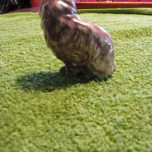 May include: A brown ceramic figurine of a cat sitting on a green rug.