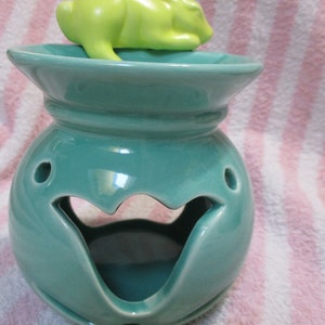 May include: Teal ceramic oil burner with a green ceramic bunny on top. The burner has a decorative cutout in the front and two small holes on the side.
