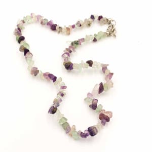 May include: A necklace made of small, irregular, light green, purple, and white gemstone chips. The necklace is strung on a silver chain.