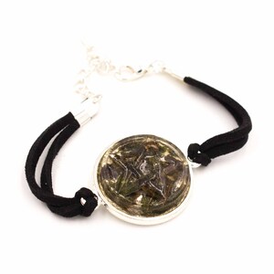 May include: A black suede bracelet with a silver-toned chain and clasp. The focal point is a round, silver-toned pendant with a five-pointed star design in shades of green and brown.