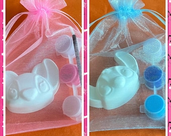 Op de afbeelding: Twee doe-het-zelf-schildersets, elk in een transparante zak met een trekkoord. Eén set bevat een wit katvormig figuur met roze verf, de andere een witte konijn met blauwe verf. Elke set bevat een penseel.