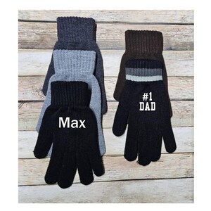 May include: Two pairs of black knit gloves with gray and brown knit cuffs. One pair has the text "Max" embroidered on the back of the hand and the other pair has the text "#1 DAD" embroidered on the back of the hand.