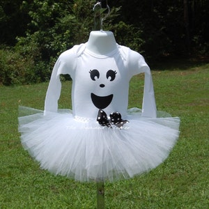 May include: White tutu with a white long-sleeved shirt featuring a black ghost face with a black and white polka dot bow. The text "The Beaded Flower" is visible on the shirt.