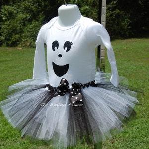 May include: White long-sleeved shirt with a black ghost face design and a black and white tulle tutu with a black polka dot bow.