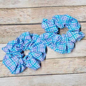 May include: Two blue and purple checkered scrunchies. The scrunchies are made of fabric and are tied together.