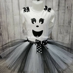 May include: White long-sleeved shirt with a black ghost face design and black polka dot bows on the shoulders. A black and white tulle tutu with a black polka dot bow.